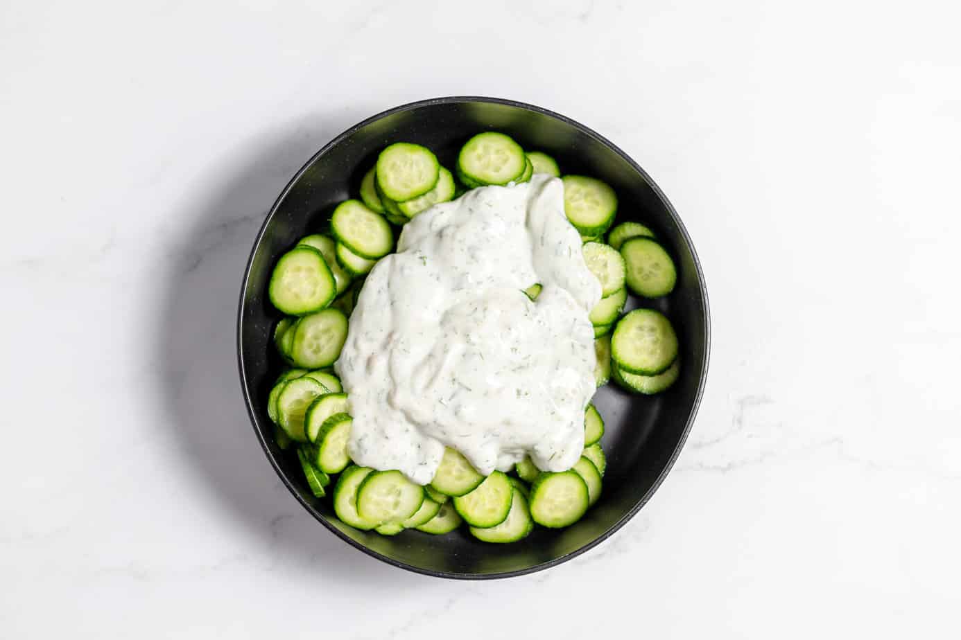 german salad dressing poured over sliced cucumbers in a black bowl